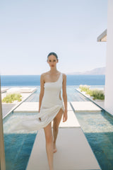 Woman in a white dress standing by a pool with ocean view