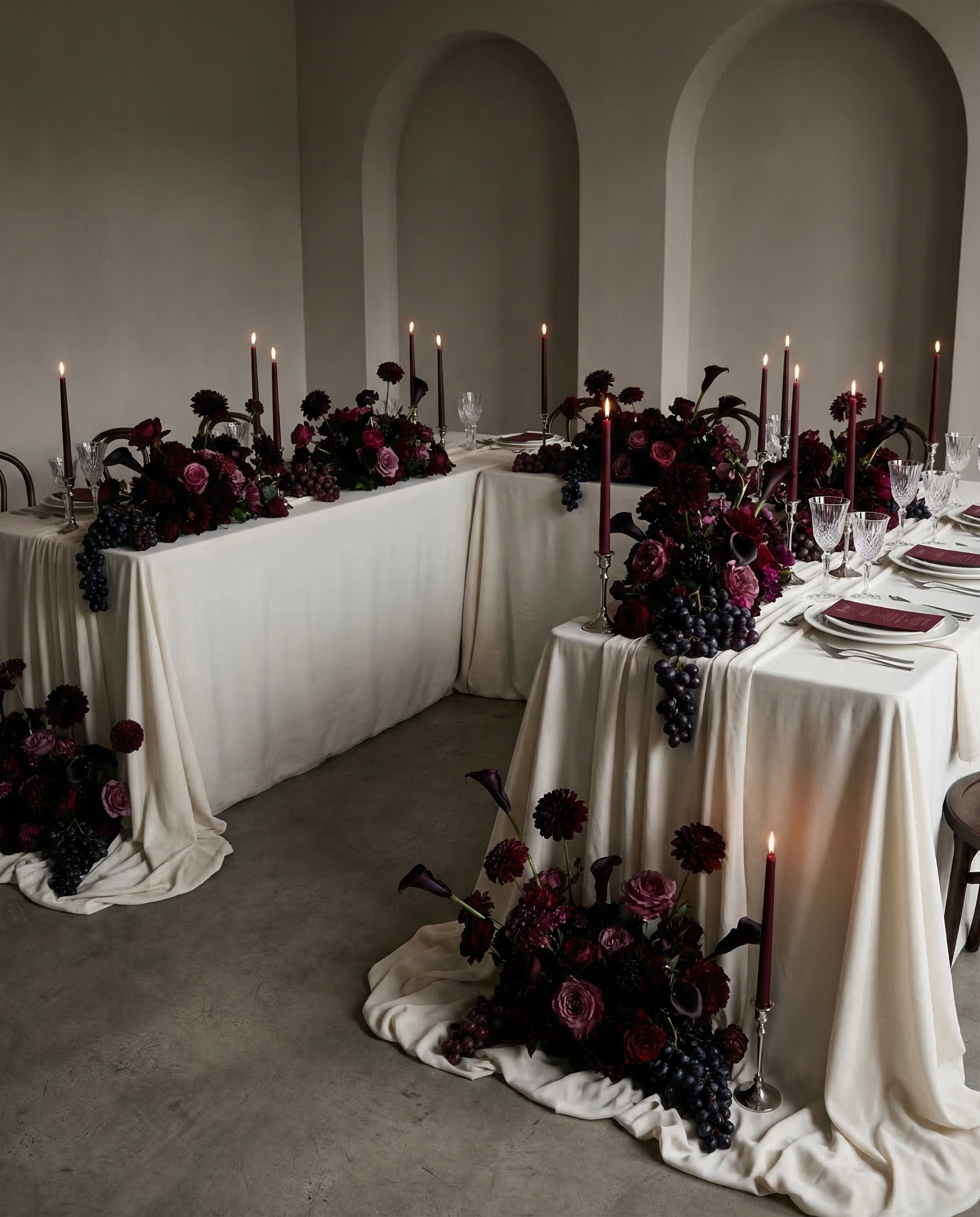 Elegant table setting with dark floral arrangements and candles in a room with arched ceilings.
